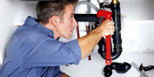 Young smiling plumber fixing a sink in the kitchen.